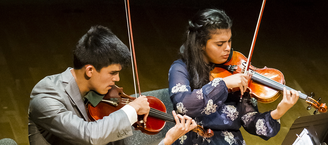 A main in a gray suit and woman in a blue dress perform with violins