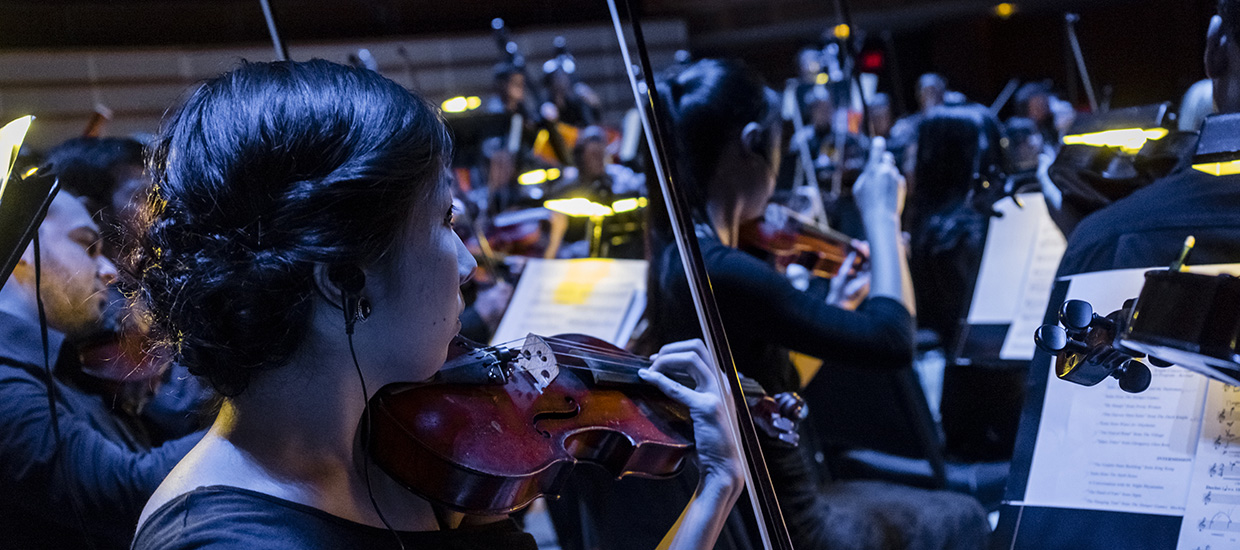 A woman with dark hair plays the violin along with the other musicians during a performance