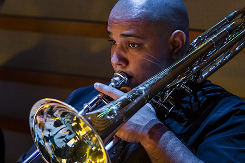 A man in a dark suit playing the trombone