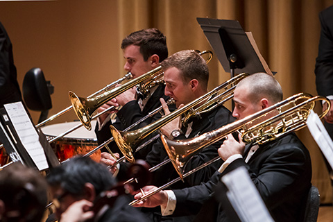 Three trombone players in dark suits perform during a live event